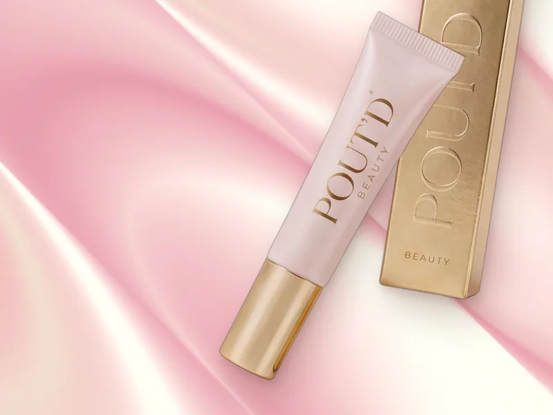 POUT'D Lip Plumper tube and gold box on pink silk, a high-shine lip plumper for a fuller-looking overlined pout, $25.